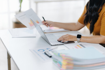 Productivity and Analysis: A focused professional meticulously analyzes financial reports while working on a laptop at a bright office desk, a picture of dedication and analytical rigor.