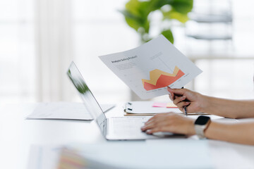 Analyzing Data: A focused individual analyzes financial data on a laptop, a document of charts held aloft, signifying deep contemplation and analysis. The setting, a modern office space.