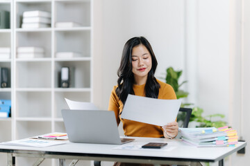 Focused Analysis: A woman, surrounded by documents, thoughtfully examines paperwork, highlighting the attention to detail and dedication within a professional office environment.