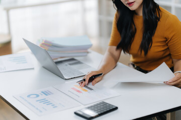 Focused and Professional: A detail-oriented woman at her desk, surrounded by documents and a laptop, embodies dedication in a modern office setup. 