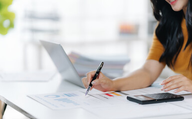 Focused Productivity: A woman meticulously examines financial documents, her attention fully engrossed. The modern workspace setting features a laptop and smartphone.