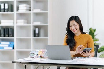 Smiling Accountant: An asian woman at desk using calculator with laptop, symbolizing business and financial activities. 