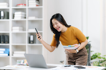 Joyful Breakthrough: A cheerful woman, phone in hand, celebrates a successful moment, surrounded by office tools, signifying a moment of achievement and happiness in a work context.