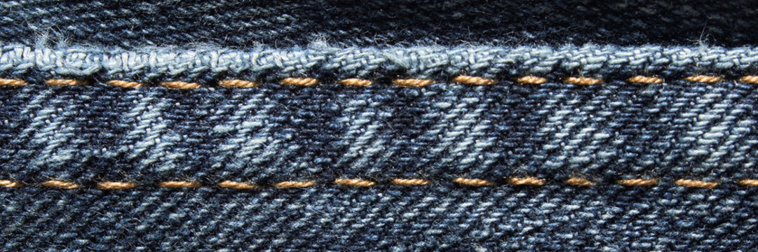 Close-up of blue denim fabric with yellow stitching detail and texture visible.