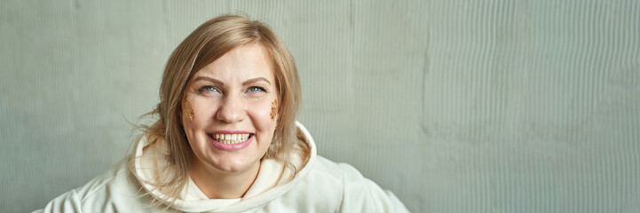 Smiling caucasian female adult in white hoodie against light background with glitter highlighting...