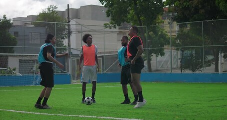 Four young men on soccer field preparing for game, warming up and stretching with ball nearby, showing teamwork, camaraderie, and focus before friendly match outdoors - Powered by Adobe