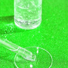 Clear dropper and beaker on sparkling green surface in laboratory setting.