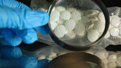Police investigator in blue gloves studying seized illegal drugs packed in vacuum bag. Forensic science criminalistics. Drugs in shape of pills seized by police. Crime scene and evidence.