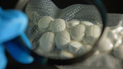 Police investigator in blue gloves studying seized illegal drugs packed in vacuum bag. Forensic science criminalistics. Drugs in shape of pills seized by police. Crime scene and evidence.