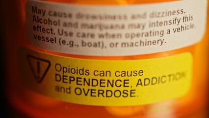 Prescription bottle full of pills with warning stickers saying, Opioids can cause dependence,...