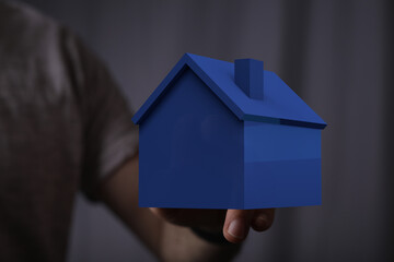 A person's hand holding a blue model house. Conceptual image for real estate, home ownership,...