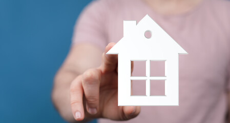 A person holds a white house symbol, representing homeownership, real estate, and the dream of owning a property. Perfect for illustrating conce