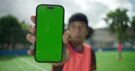 Hispanic man on soccer field holding smartphone with green screen close to camera, blurred background, concept for mobile app or digital product mockup, technology, outdoor lifestyle - Powered by Adobe