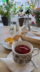 Cup of hot tea with steam on a wooden table in a cozy cafe. Morning breakfast with cookies, honey, and plants in the background. Warm atmosphere and natural daylight