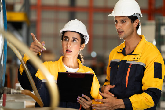 Female and male engineers in safety uniforms discussing fluid system inspection at factory. Industrial teamwork, engineering process, and workplace safety in manufacturing. engineer, two worker.