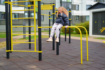 girl enjoying playground activity, balancing on outdoor gym equipment. urban park scene with yellow bars, showcasing active lifestyle and childhood play in modern residential area