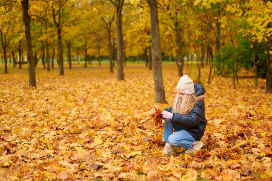 young woman in autumn park gathering colorful leaves. seasonal nature adventure capturing essence of fall foliage with vibrant golden scenery. perfect for themes of outdoors and tranquility