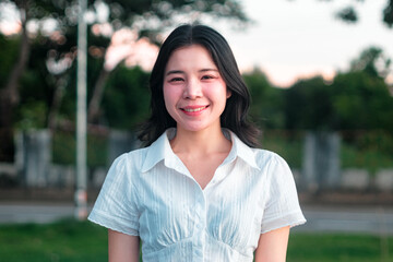 Young woman smiling outdoors in a vibrant green park setting under soft natural light