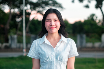 Young woman smiling outdoors in a vibrant green park setting under soft natural light with trees and a peaceful background atmosphere