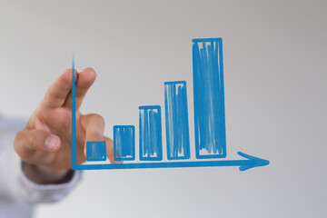 Business growth concept: a hand sketching a rising bar chart on a transparent surface, representing progress and success.