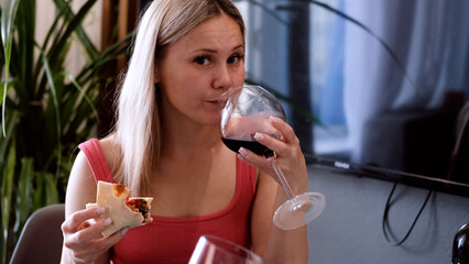 A woman eats pizza and drinks red wine as she enjoys a casual meal in the kitchen