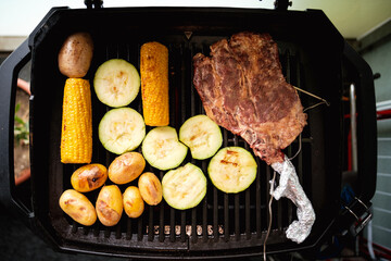Tomahawk Steak, Maiskolben, Zucchinischeiben und Kartoffeln am Grill