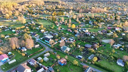 Aerial view of an autumn landscape in Estonia featuring a cozy countryside cottage in the foreground and a colorful forest in the background.