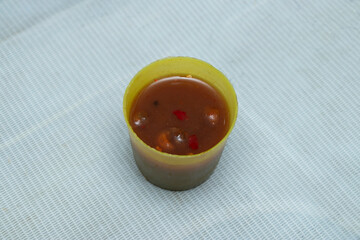 Spicy Chutney Sauce, Misti Tok flavorful savory broth brimming with tender morsels and bright chili flakes, perfectly portioned in a handy yellow cup for an irresistible culinary delight.