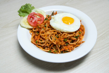 Special Chowmein spaghetti dish topped with a perfectly fried egg and vibrant fresh vegetables, elegantly presented in a white bowl on a light wooden surface for a delightful meal experience.