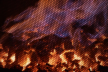 Feu de cheminée abstrait vu à travers une grille métallique – texture chaude, lumière orangée et flammes en arrière-plan
