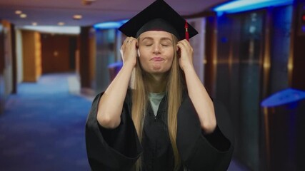 Woman in graduation cap with humorous expression indoors at a hotel corridor illustrating a moment of surprise and achievement captured in vivid detail.