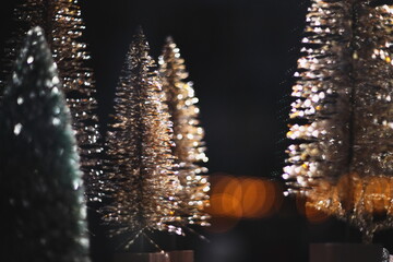 Artistic close-up of sparkling miniature Christmas trees with beautiful bokeh lights, creating a...