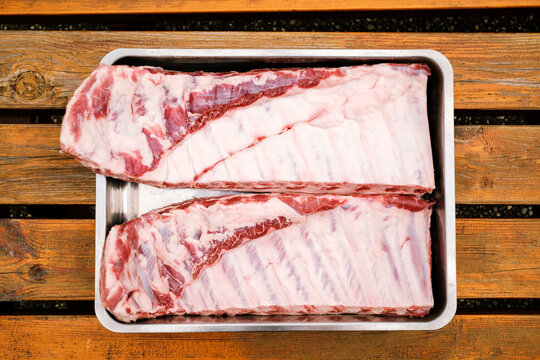 St. Louis Cut Ribs (fleischige Bauchrippen vom Schwein) in Edelstahlbr&auml;ter auf Holztisch