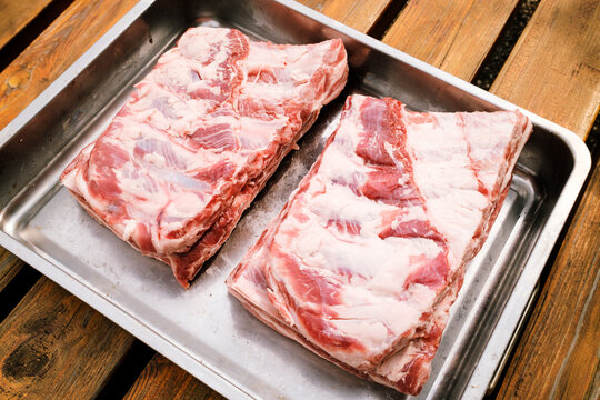 St. Louis Cut Ribs (fleischige Bauchrippen vom Schwein), halbiert in Edelstahlbr&auml;ter auf Holztisch