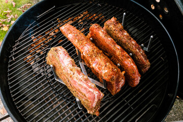 St. Louis Cut Ribs (fleischige Bauchrippen vom Schwein), halbiert, gewürzt in Rippchenhalter auf Grillrost im Kugelgrill