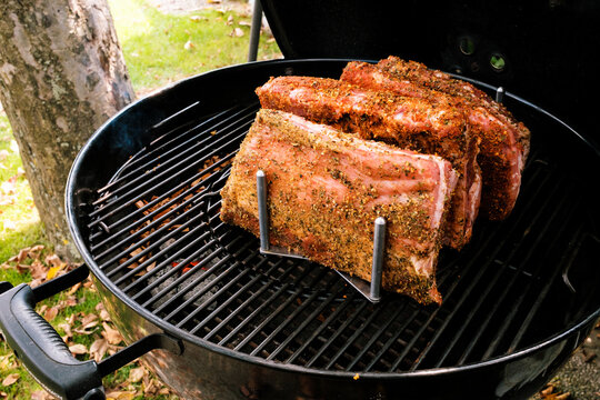 St. Louis Cut Ribs (fleischige Bauchrippen vom Schwein), halbiert, gew&uuml;rzt in Rippchenhalter auf Grillrost im Kugelgrill