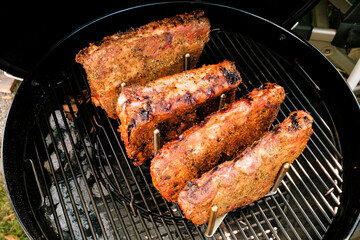 Geräucherte St. Louis Cut Ribs (fleischige Bauchrippen vom Schwein) in Rippchenhalter am Grillrost im Kugelgrill