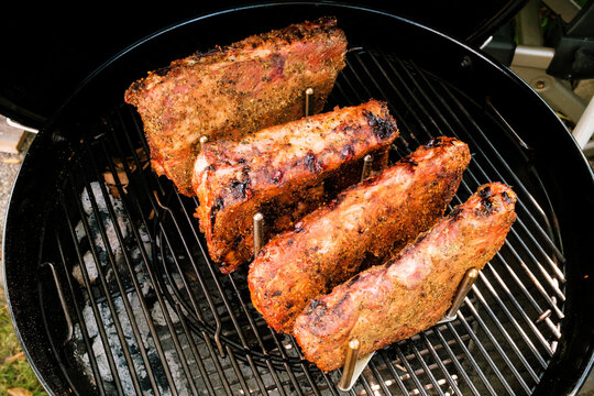 Ger&auml;ucherte St. Louis Cut Ribs (fleischige Bauchrippen vom Schwein) in Rippchenhalter am Grillrost im Kugelgrill