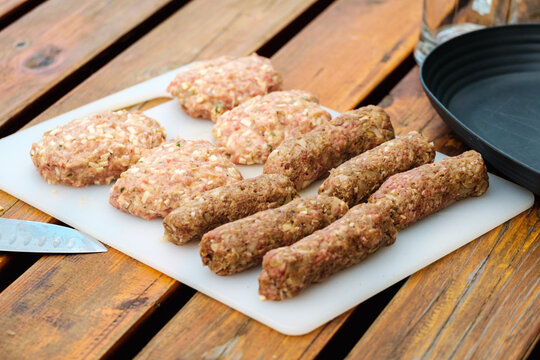 rohe Bifteki (Fleischlaibchen) und Cevapcici auf wei&szlig;em Kunststoffbrett auf Holztisch