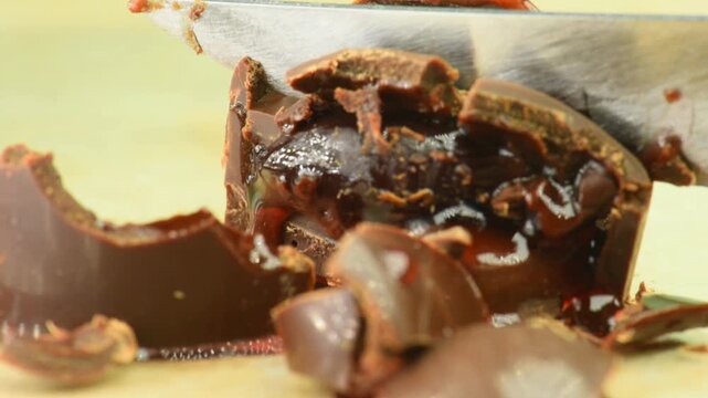 Cutting a chocolate candy with a knife, the filling with liqueur and cherry flows out of the candy, close-up.