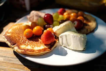 Zwei Pancakes mit Beeren (Physalis, Weintrauben und Erdbeeren) und Eiscreme (Vanille, Nougat und Pistazie) auf Teller am Holztisch