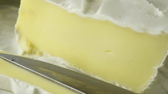 Cutting soft cheese with white mold with a knife, close-up, creamy texture and edible mold close-up.