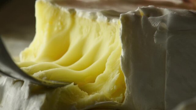 A close-up of soft French Camembert cheese being picked up with a fork, showing the creamy texture and edible mold.