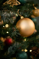 Closeup showing decorated Christmas tree with gold ornaments hanging among pine needles, blurred lights glowing softly in background, festive holiday setting