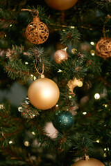 Closeup showing decorated Christmas tree branches with gold and green baubles, glittering ornaments and warm string lights hanging among green pine needles during holiday season