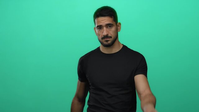 Hispanic man in black shirt pointing with focus against a solid green background, showcasing his confident and attractive demeanor.