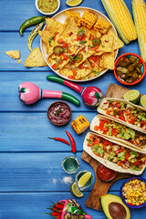 Set of various traditional mexican food on blue wooden background. Tacos, nachos, corn cobs, grilled corn, tequila shots, vegetables and sauces, maracas. Top view, flat lay