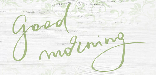 Green handwritten Good Morning typography on white wooden background with soft decorative pattern