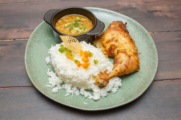 Yassa poulet – poulet mariné aux oignons et citron, plat traditionnel ouest-africain présenté sur une assiette colorée, table en bois. Plat africain. 