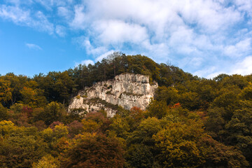 Majestic white limestone rock rises above a dense green forest under a blue sky with clouds. The...